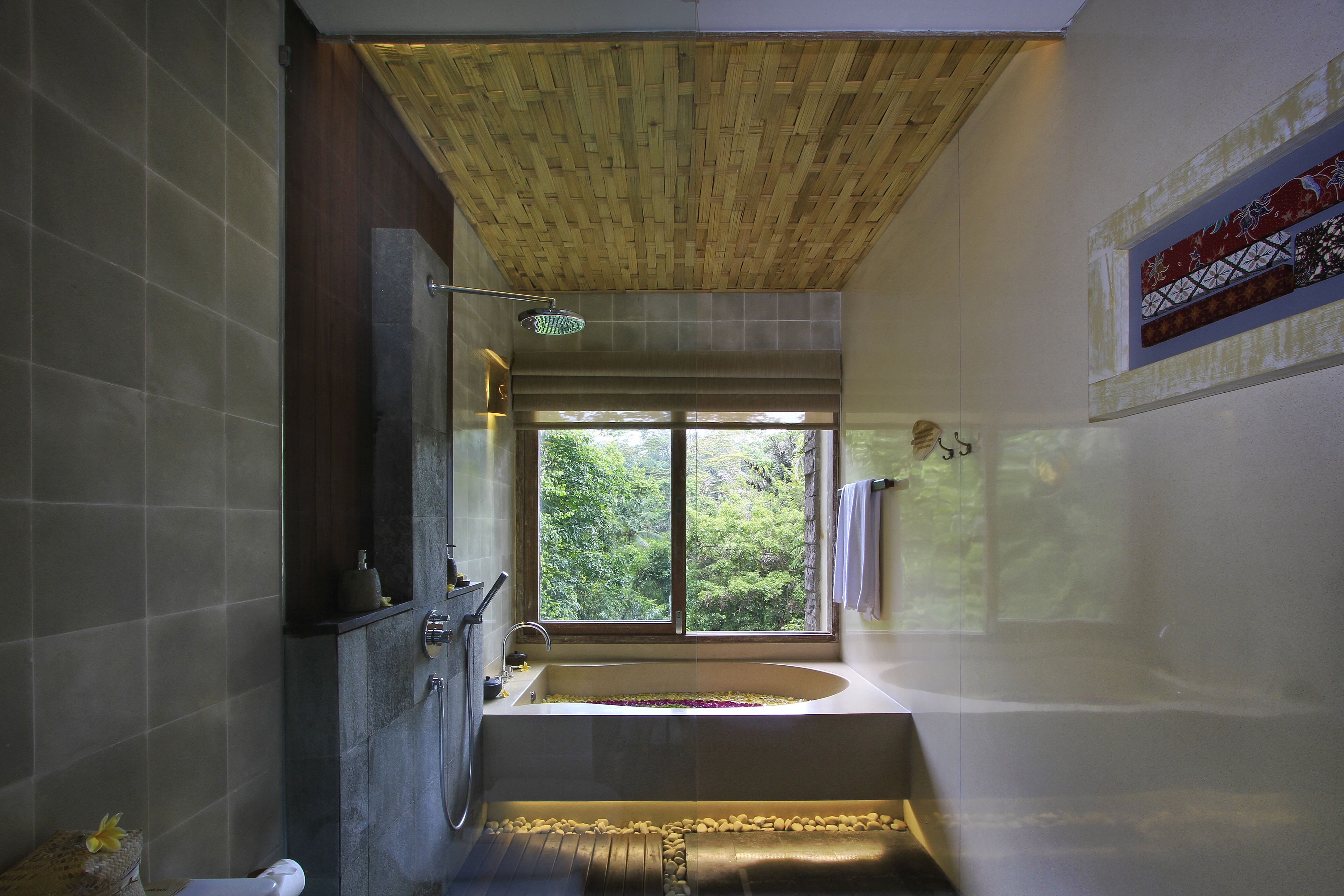A modern bathroom with a large bathtub, a shower, and a window providing a view of greenery.