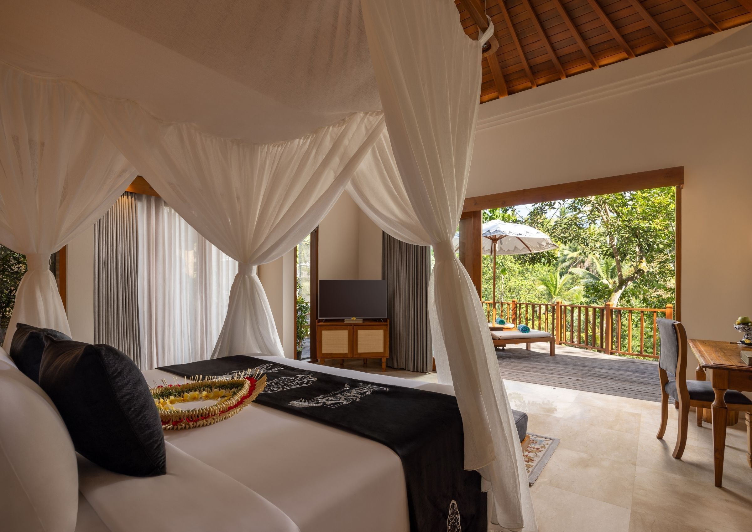 A bedroom with a canopy bed, a TV, and a balcony with a table and chairs.