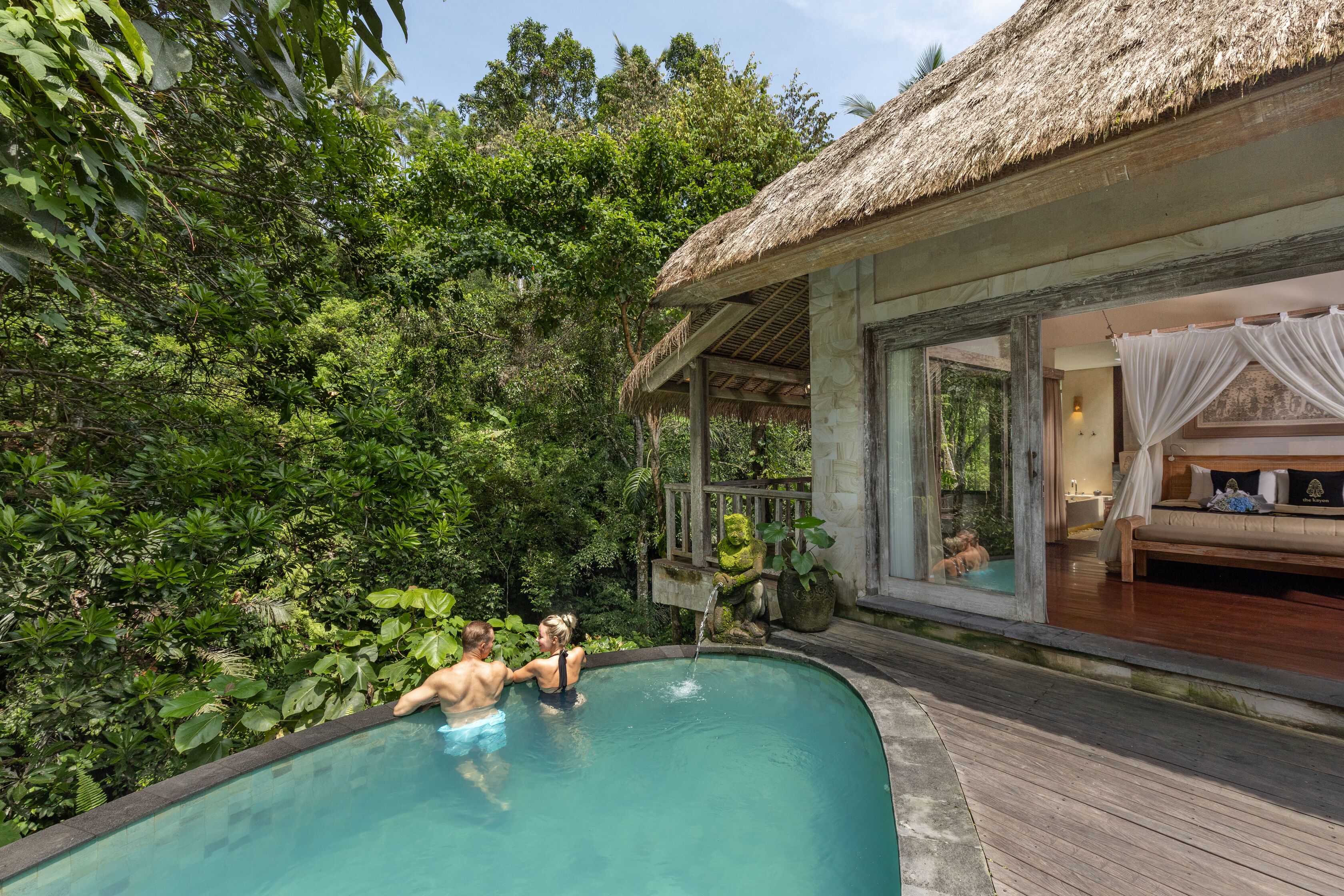 A private pool with a thatched roof structure, surrounded by lush greenery.