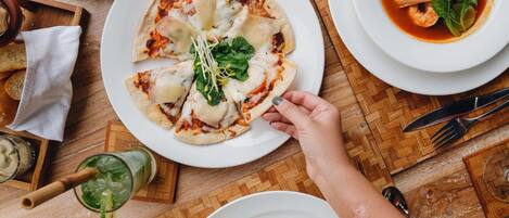 A dining table with a menu, plates of food including pizza, soup, and a burger, and a glass of drink.