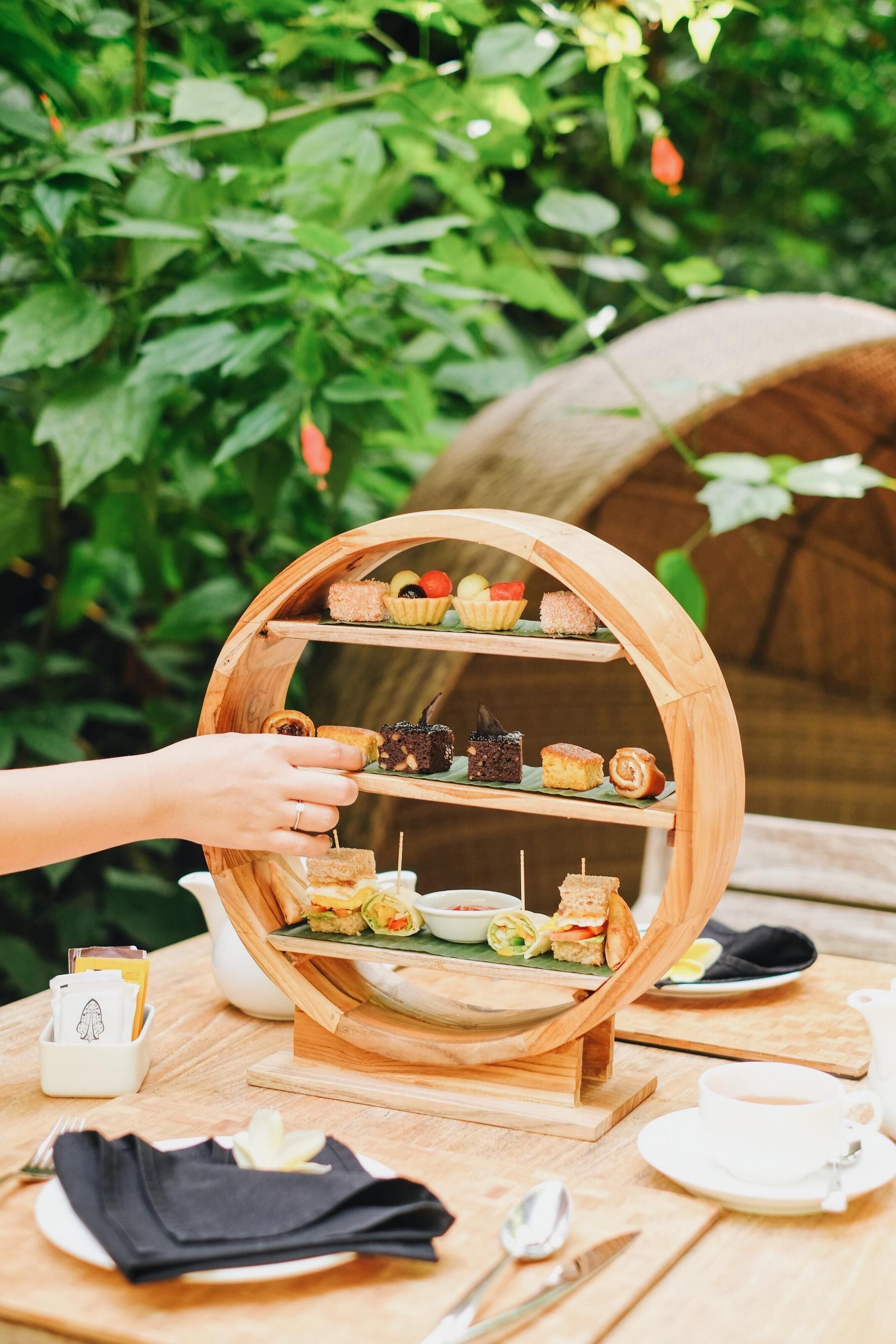 Un chariot en bois rempli de diverses pâtisseries et de sandwichs, placé sur une table à l’extérieur.