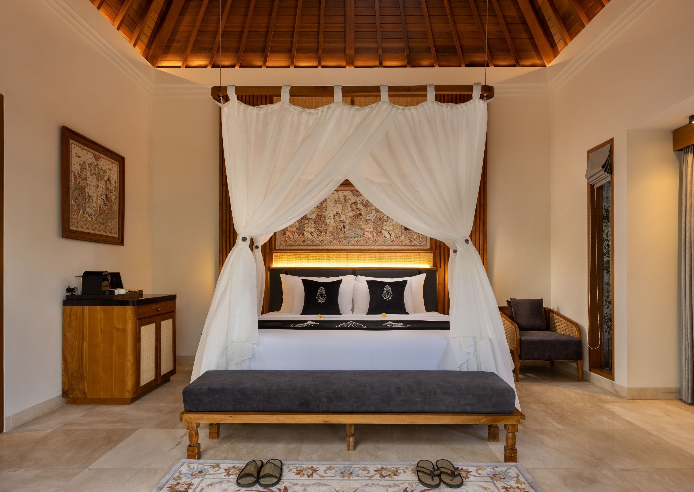 A bedroom with a canopy bed, a bedside table, a bench, and a framed picture on the wall.