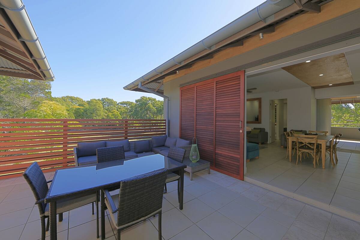 An outdoor patio with a dining table and chairs, a sofa, and a sliding glass door leading to an interior space.