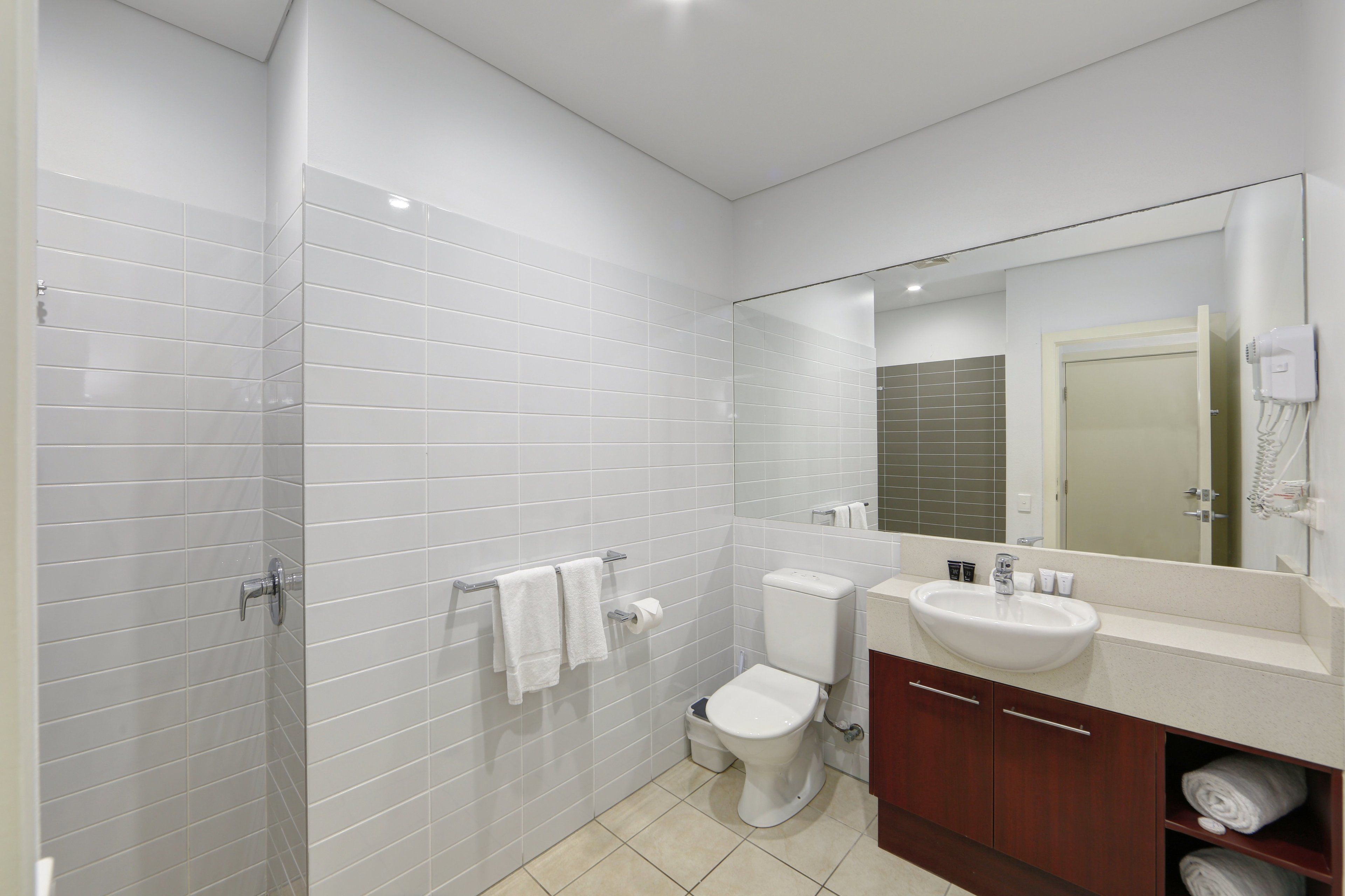 A modern bathroom with white tiles, a toilet, a sink, and a mirror.