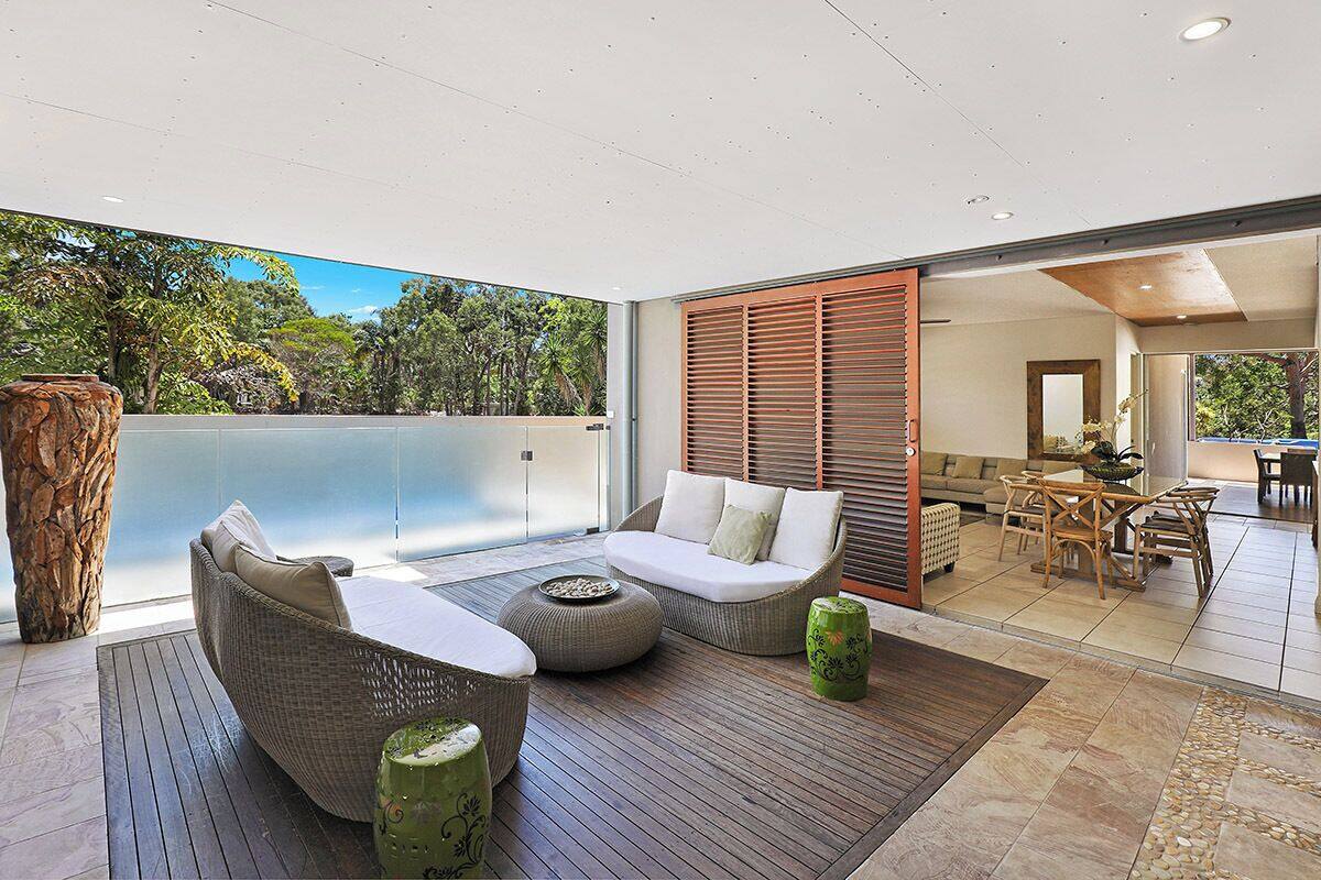 A modern outdoor living area with wicker furniture, a wooden floor, and a view of the surrounding landscape.