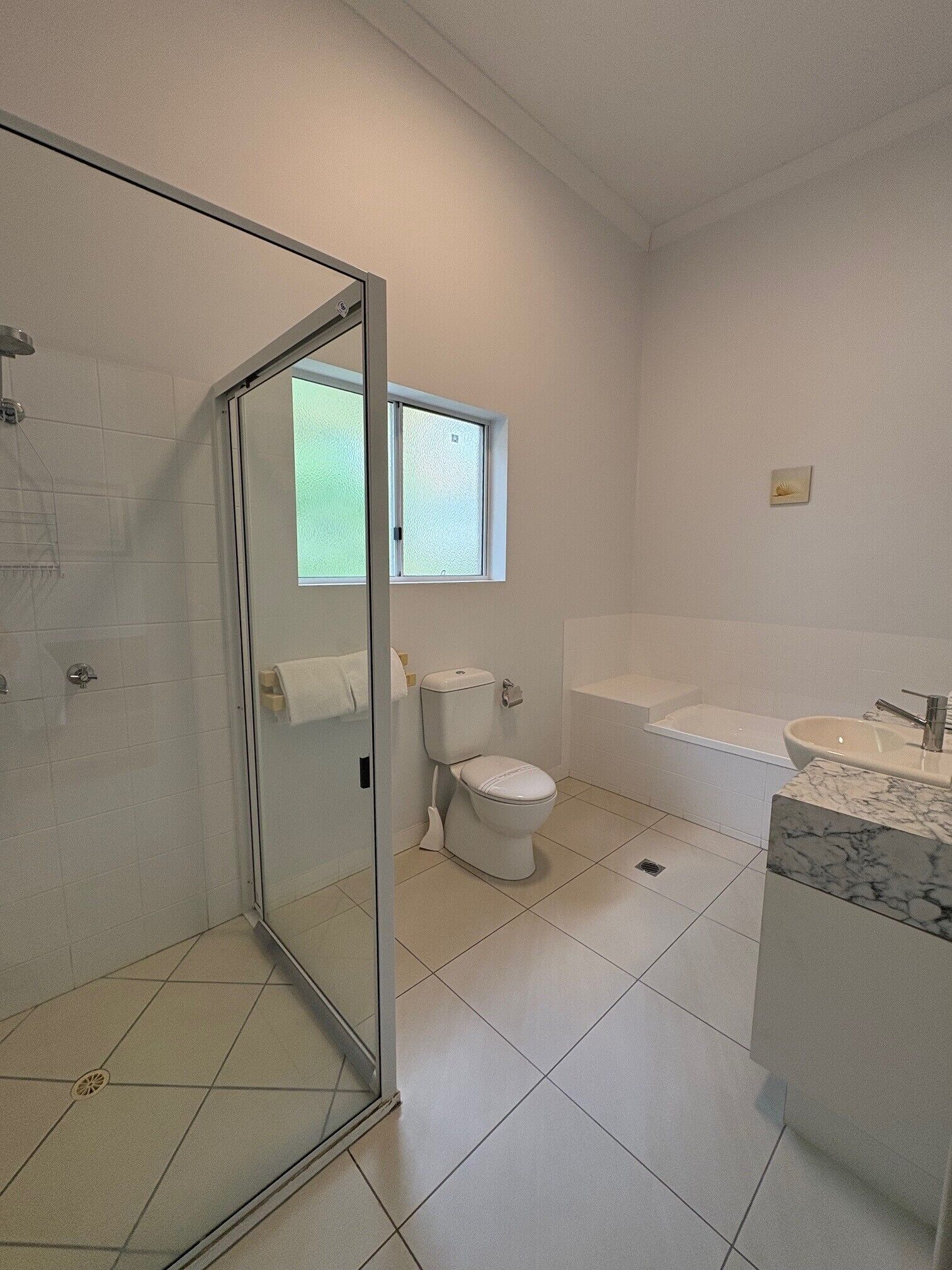 A bathroom with a glass shower enclosure, a toilet, a bathtub, and a marble sink.