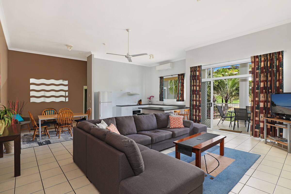 A modern living room with a sectional sofa, dining area, and a kitchen in the background.
