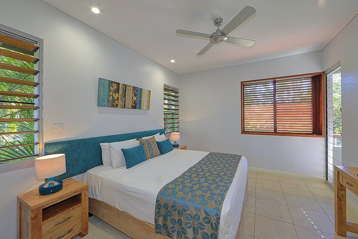 A bedroom with a bed, nightstands, a ceiling fan, and a window with blinds.