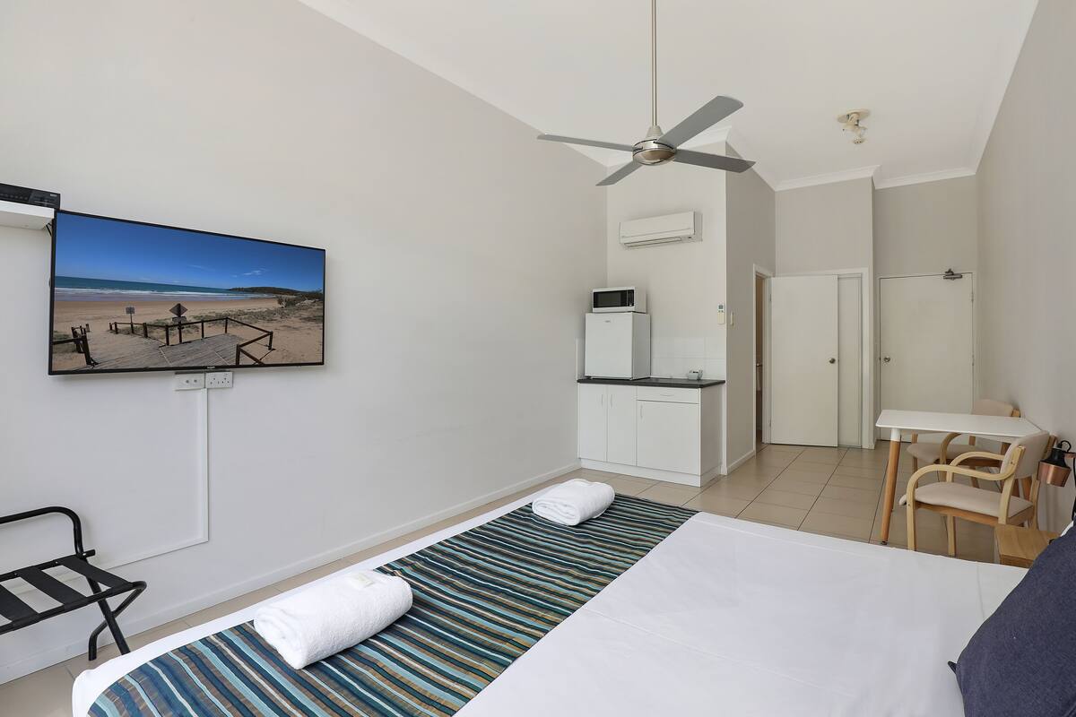 A hotel room with a bed, a desk, a chair, a television, and a ceiling fan.