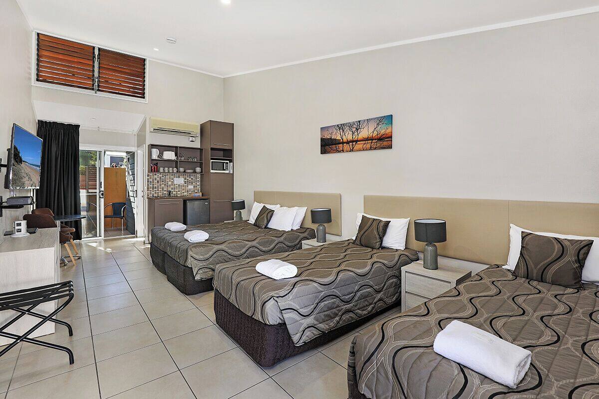 A hotel room with three beds, a desk, a chair, a TV, and a painting on the wall.