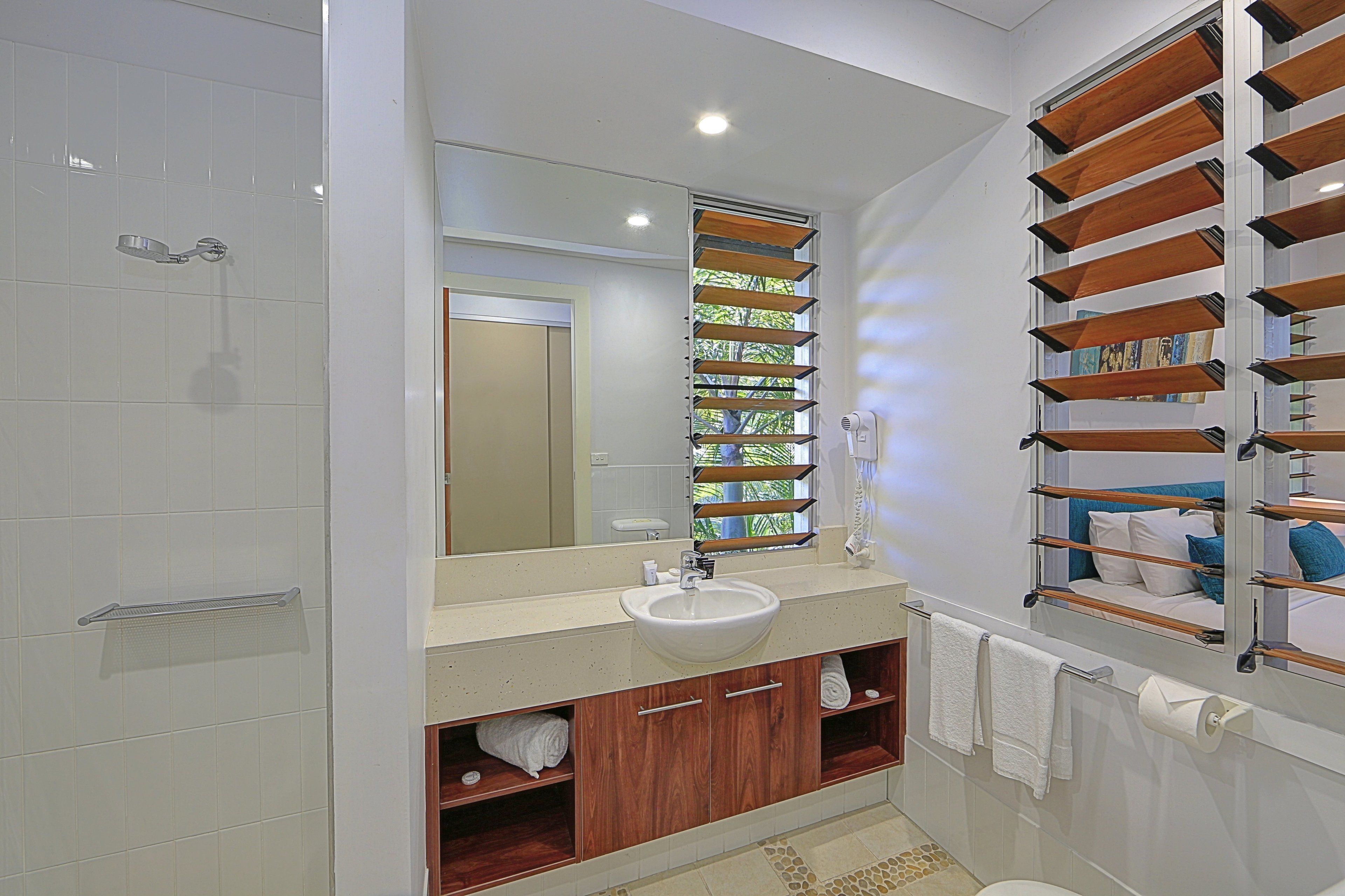 A modern bathroom with a large mirror, a sink, wooden shelves, and a shower area.