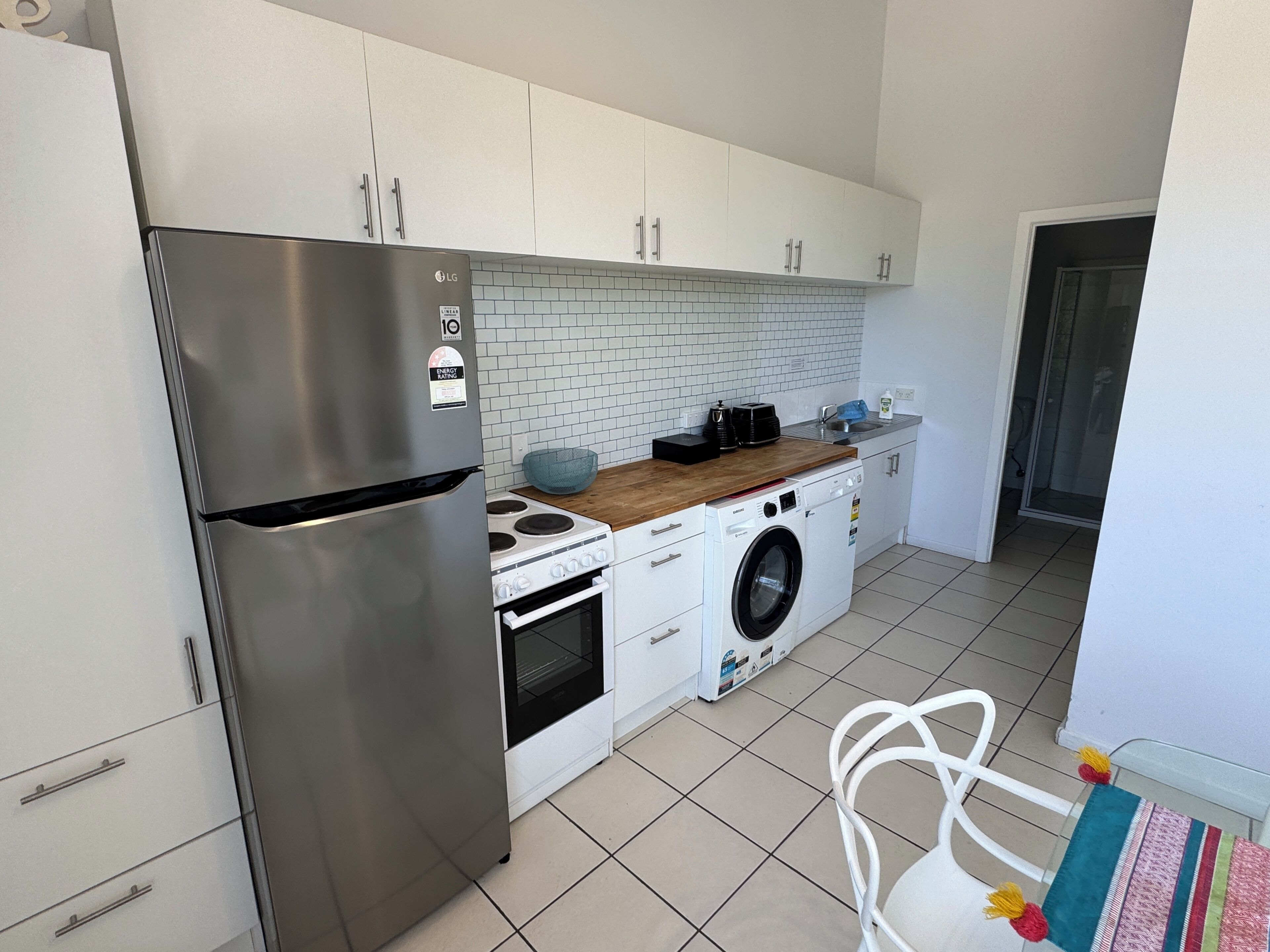 A modern kitchen with a stainless steel refrigerator, a built-in oven, a washing machine, and a tiled backsplash.