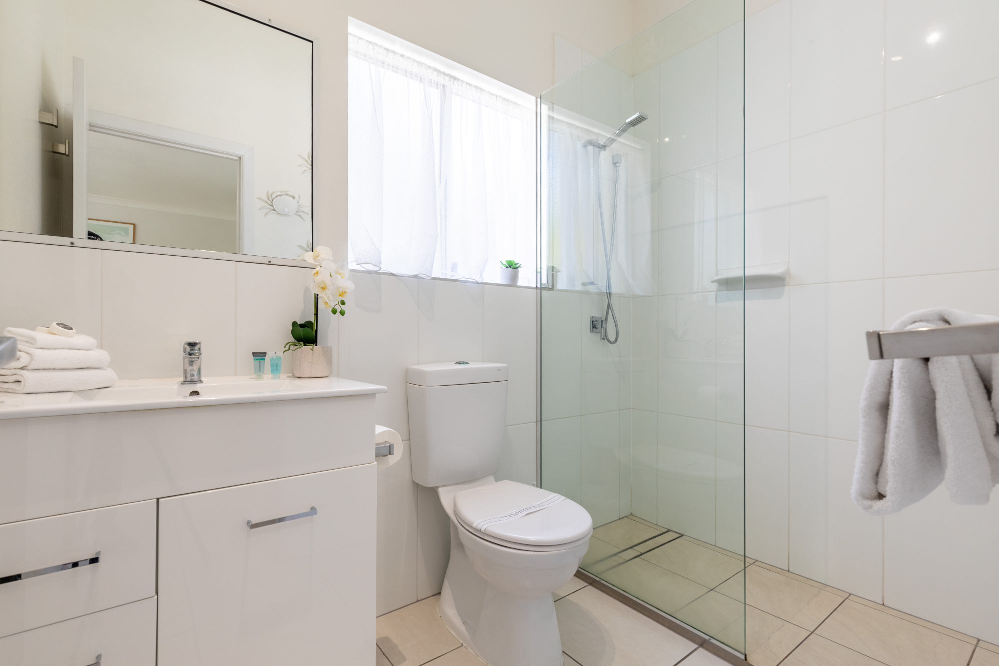 Un baño moderno con cabina de ducha de vidrio, inodoro blanco y tocador con espejo.