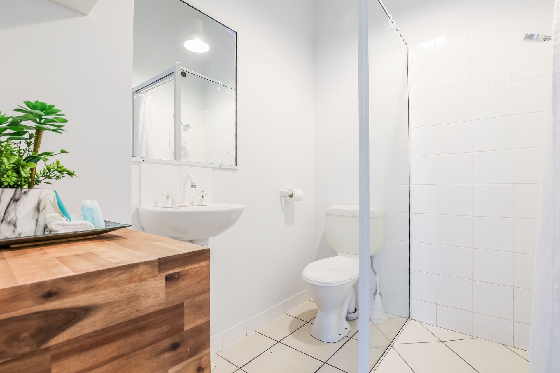 A modern bathroom with a wooden vanity, a white sink, a toilet, and a glass shower enclosure.