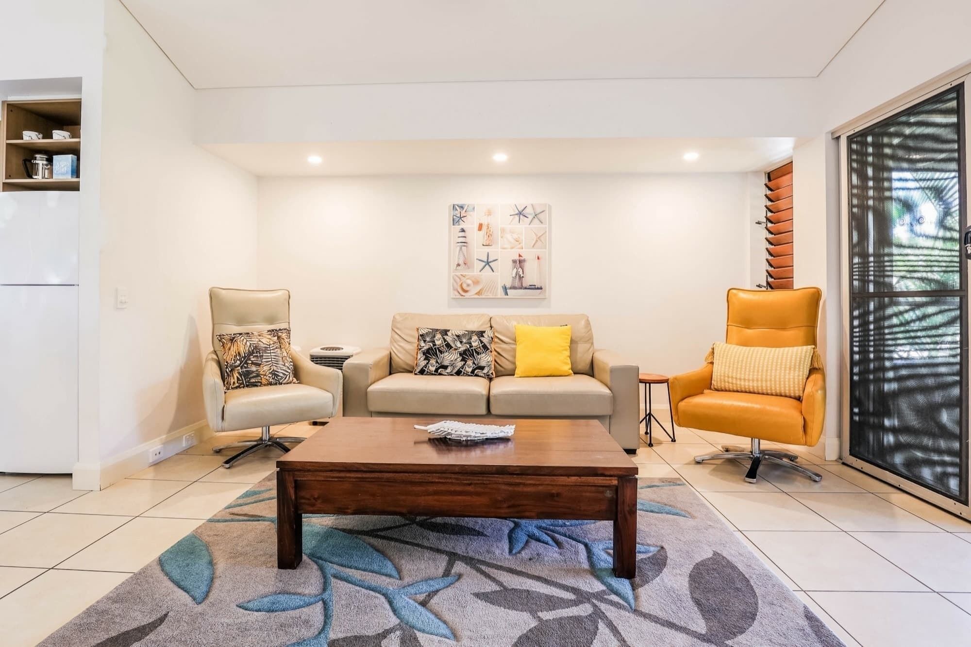 A living room with a sofa, two armchairs, a coffee table, and a large window with blinds.