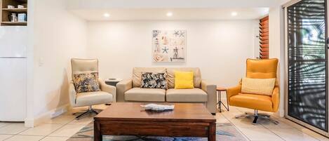 A living room with a sofa, two armchairs, a coffee table, and a large window with blinds.