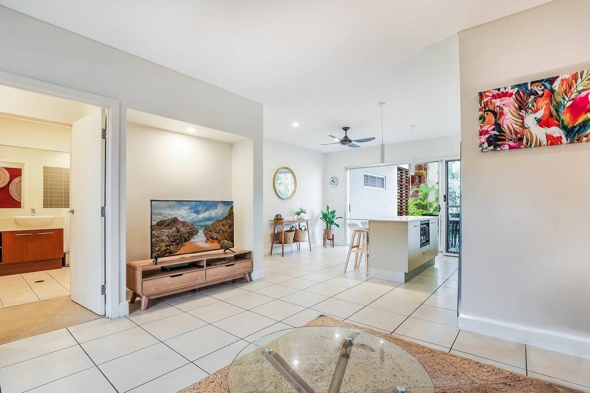 A modern living room with a large TV, a dining area, and a kitchen.