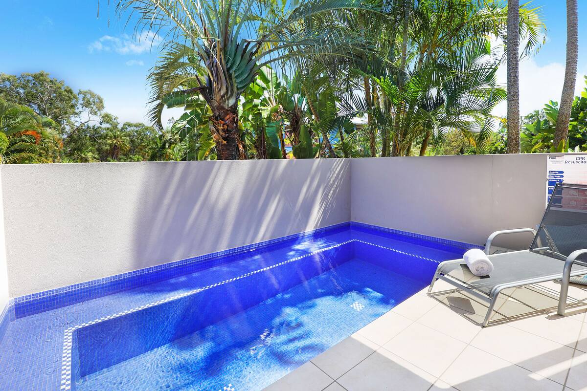 A swimming pool with a blue mosaic tile design, surrounded by a white wall and palm trees.