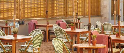 An outdoor seating area with wooden tables and chairs, some with umbrellas.