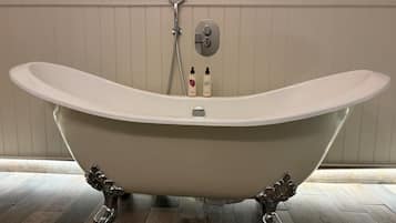 Una bañera independiente de diseño moderno, un cabezal de ducha y dos botellas de champú en el borde.