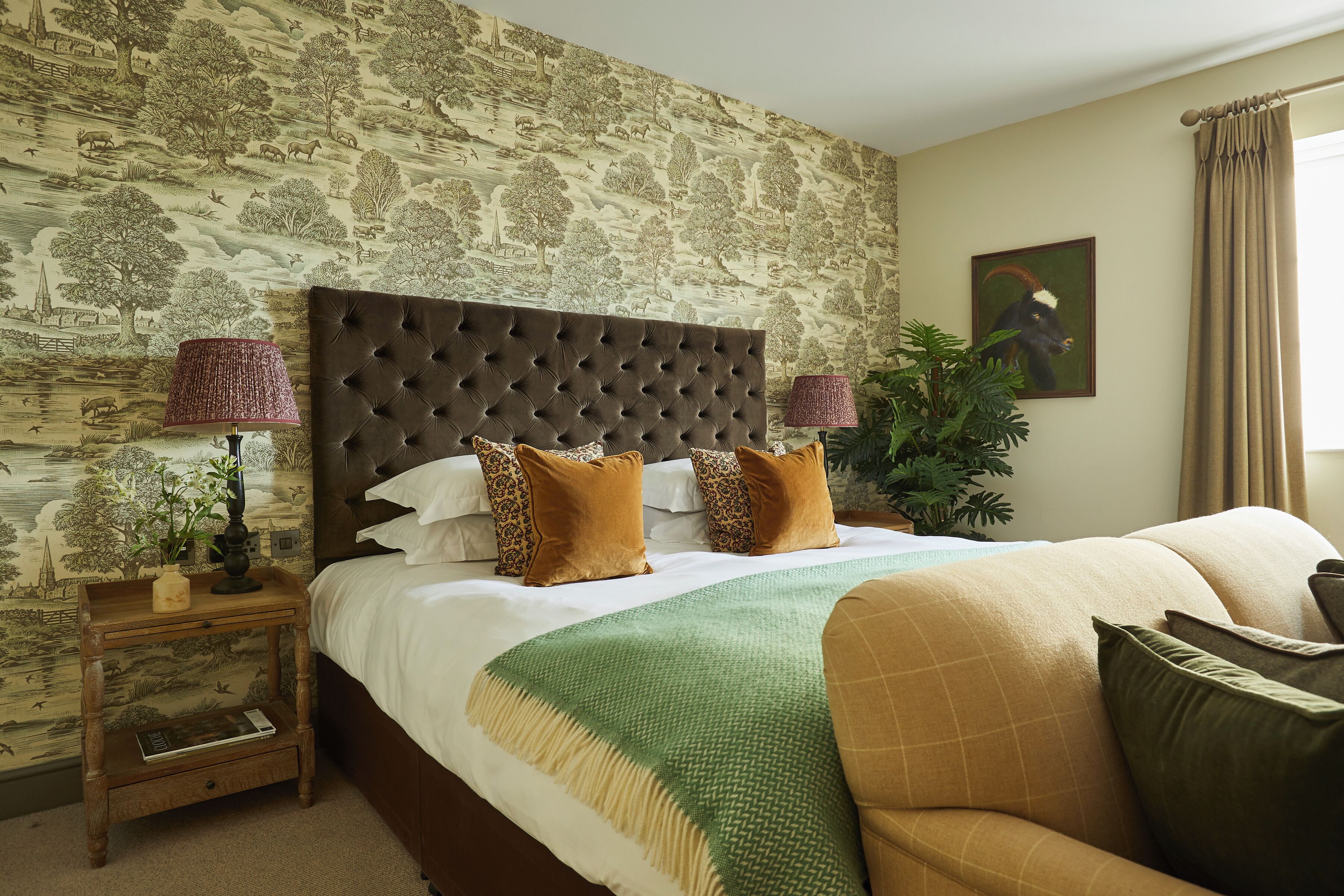 A bedroom with a large bed, a wooden nightstand, a green throw blanket, and a painting on the wall.