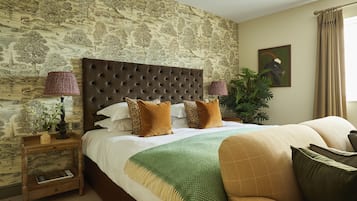 A bedroom with a large bed, a wooden nightstand, a green throw blanket, and a painting on the wall.