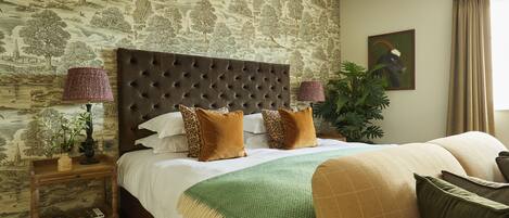 A bedroom with a large bed, a wooden nightstand, a green throw blanket, and a painting on the wall.