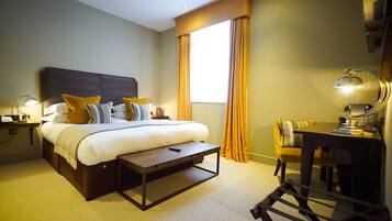 A hotel room with a bed, bedside table, lamp, desk, chair, and large window with curtains.