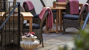 An outdoor patio with wicker furniture, a stone planter, and string lights. - Kings Head (Cirencester)