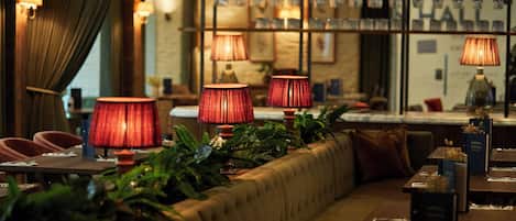 L’intérieur de ce restaurant est chaleureux, avec un long banc rembourré, des lampes rouges et une variété de plantes.