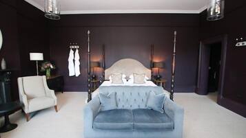 A bedroom with a four-poster bed, a light blue sofa, a white armchair, and two bedside tables with lamps.
