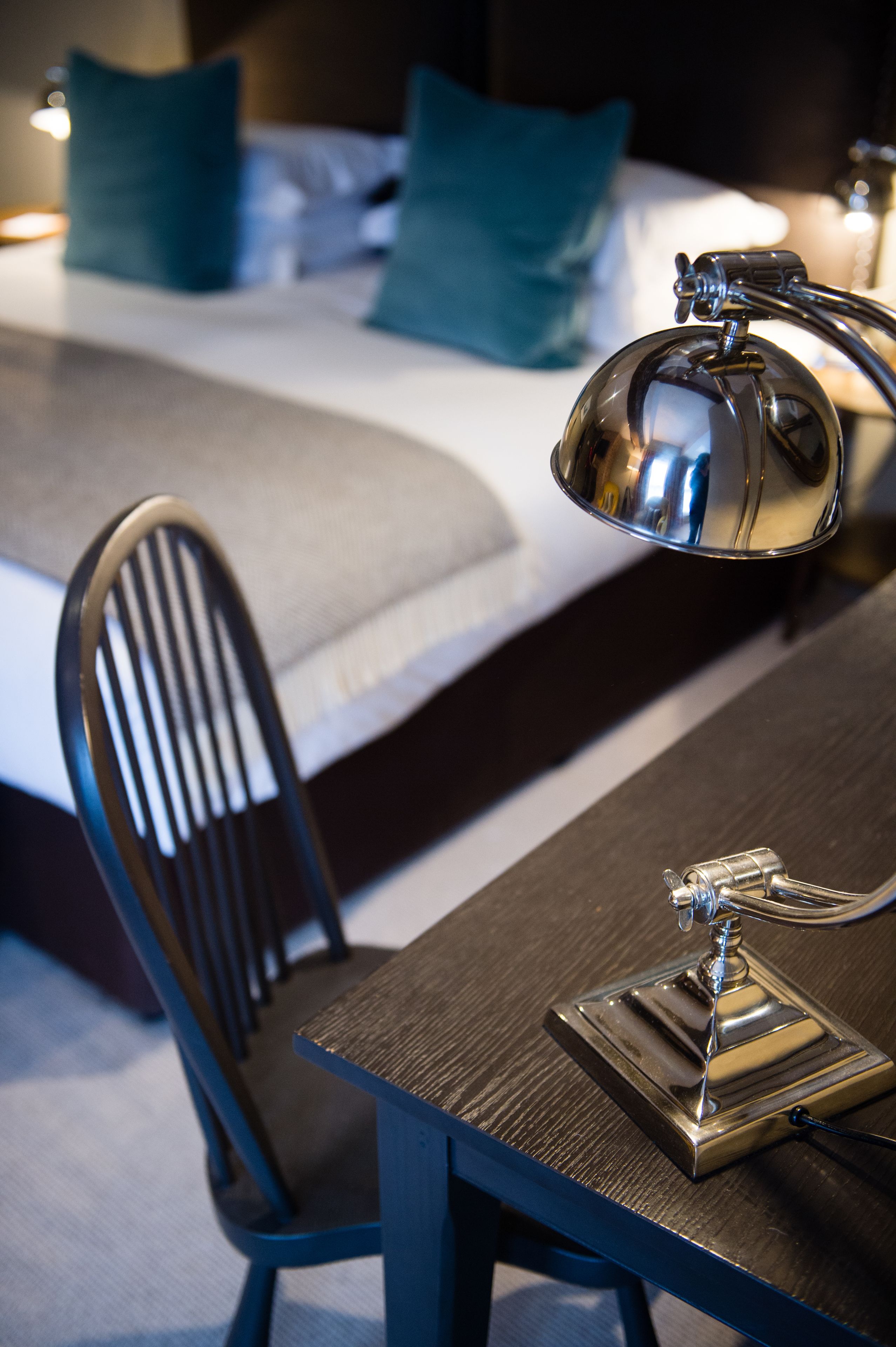 Un lit bien fait, avec une couette blanche et grise, un oreiller bleu et une table de chevet sur laquelle se trouve une lampe.