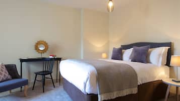 A neatly arranged hotel room with a large bed, a desk with a chair, a small table with a lamp, and a wall-mounted mirror.