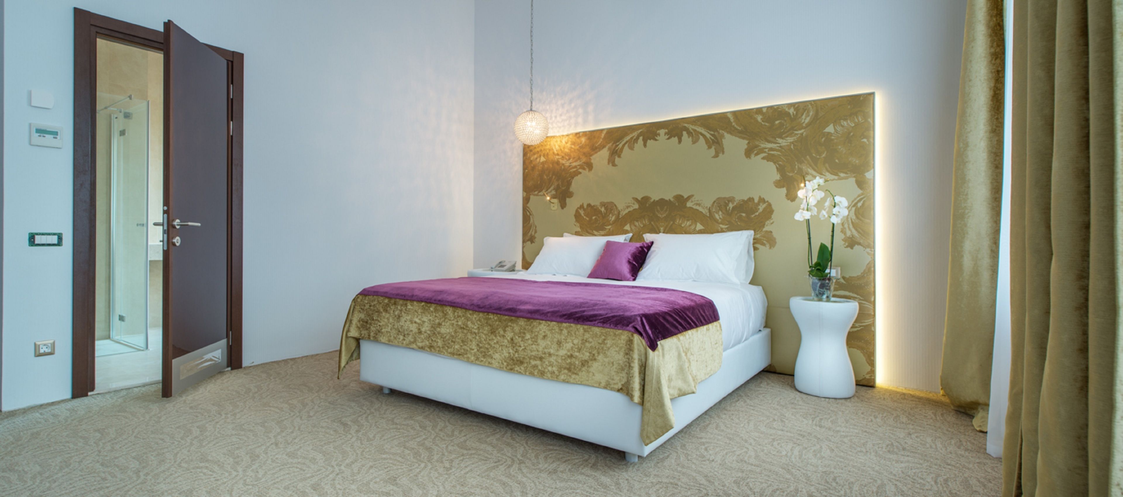 A hotel room with a bed, a bedside table with a plant, and a door leading to a bathroom.