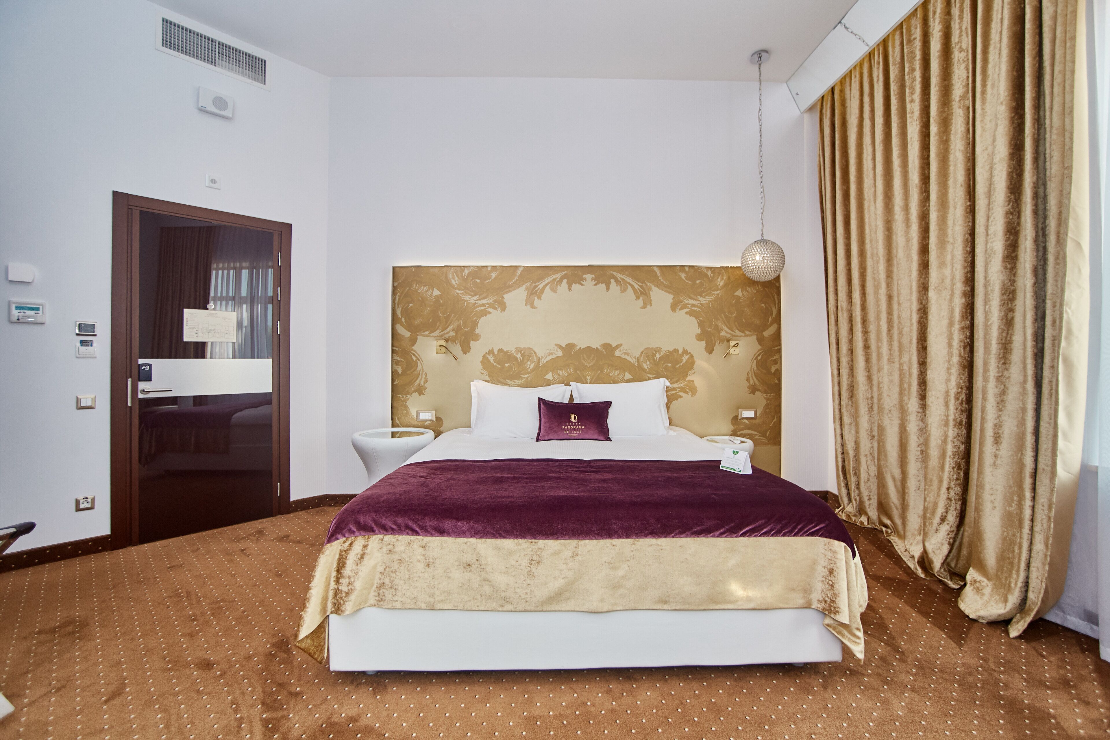 Une chambre d’hôtel avec un grand lit, une table de chevet, un miroir et une fenêtre avec des rideaux.