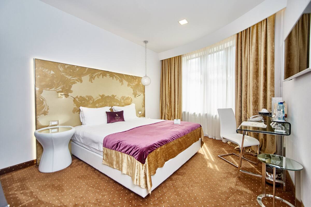 A hotel room with a large bed, a bedside table, a chair, a desk, and a mirror.