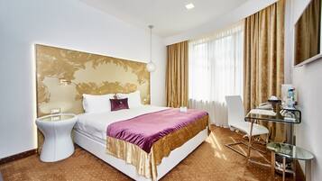 A hotel room with a large bed, a bedside table, a chair, a desk, and a mirror.
