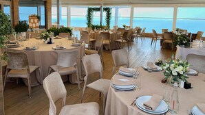 A spacious dining area with multiple tables set for guests, large windows offering a view of the sea, and string lights on the ceiling. - Panorama De Luxe (Odesa)