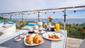 A breakfast setup with croissants, fruit, and beverages on a balcony overlooking a scenic view. - Panorama De Luxe (Odesa)