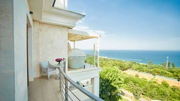 Ein Balkon mit Tisch und Stuhl, mit Blick auf eine Küstenlandschaft mit Bäumen und Meer.