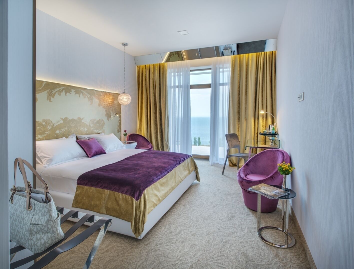 Un cuarto de hotel con cama, una silla, una mesita y vista al mar.