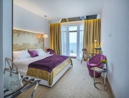 Un cuarto de hotel con cama, una silla, una mesita y vista al mar.