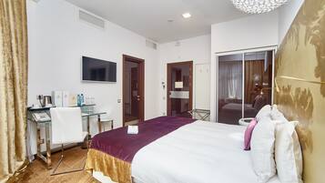 A hotel room with a bed, a desk with a chair, a TV, and a bathroom visible through an open door.
