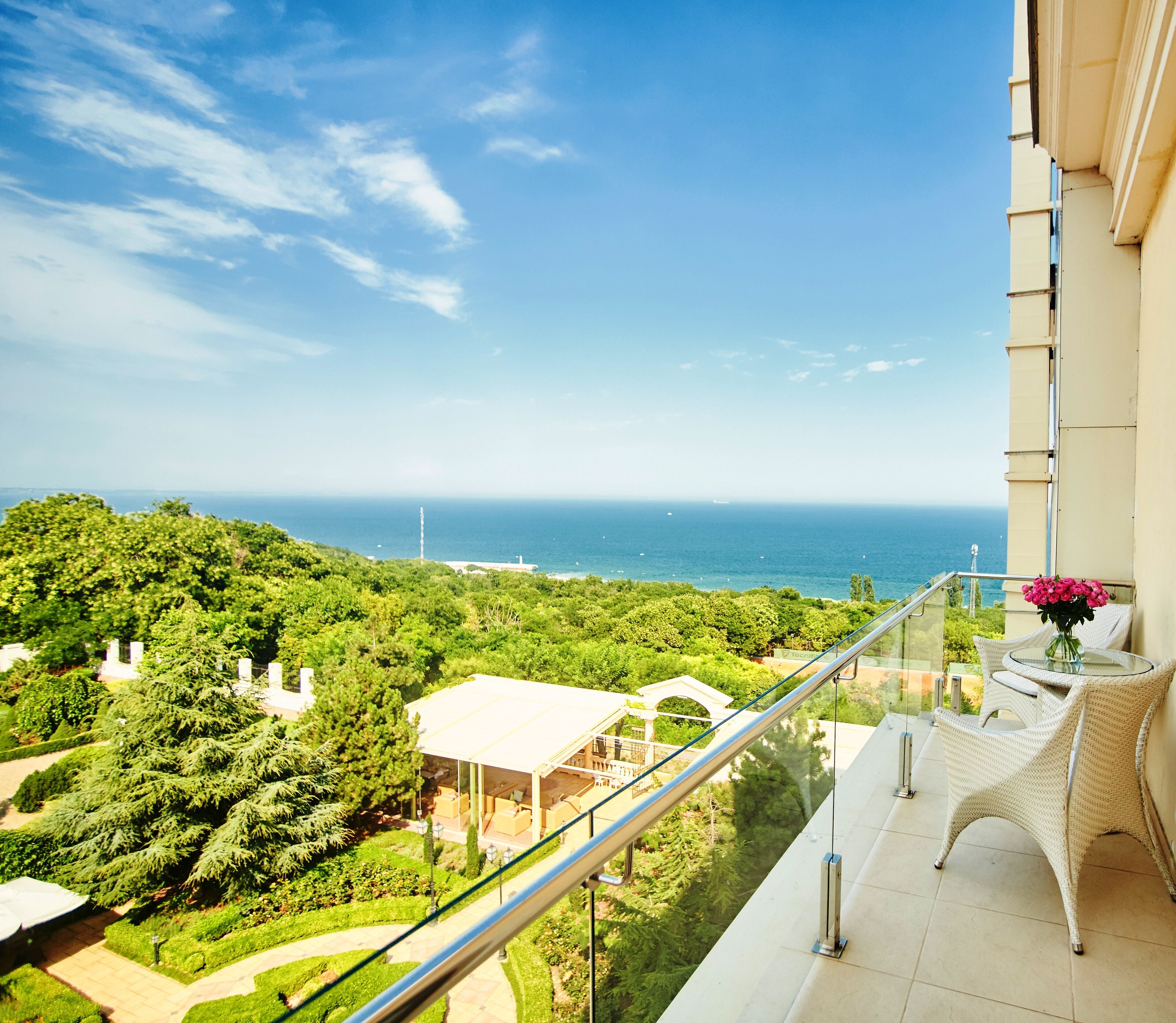 A balcony with a glass railing overlooking a lush green landscape and the sea.
