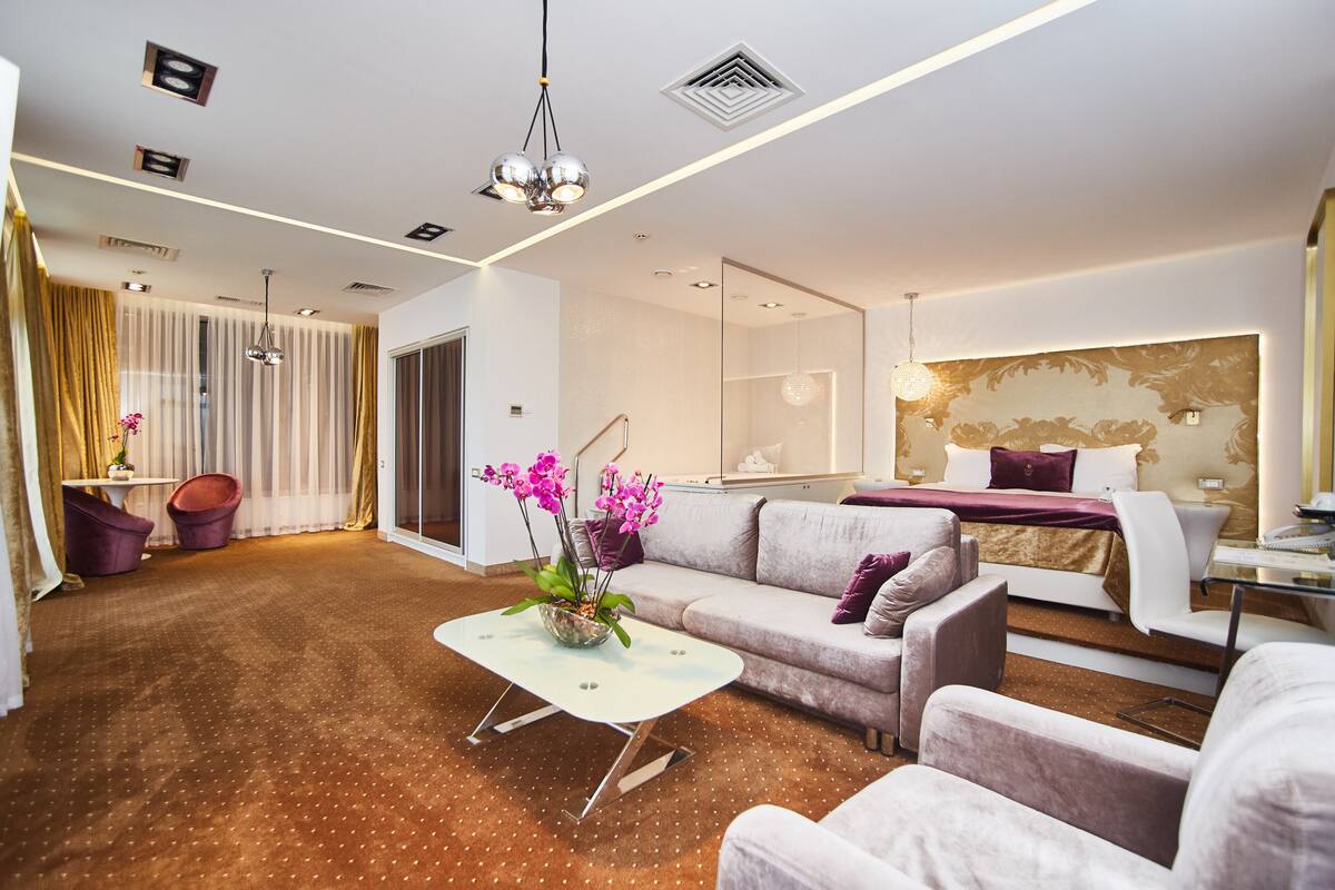 A modern hotel room with a sofa, armchairs, a dining table, and a bed.