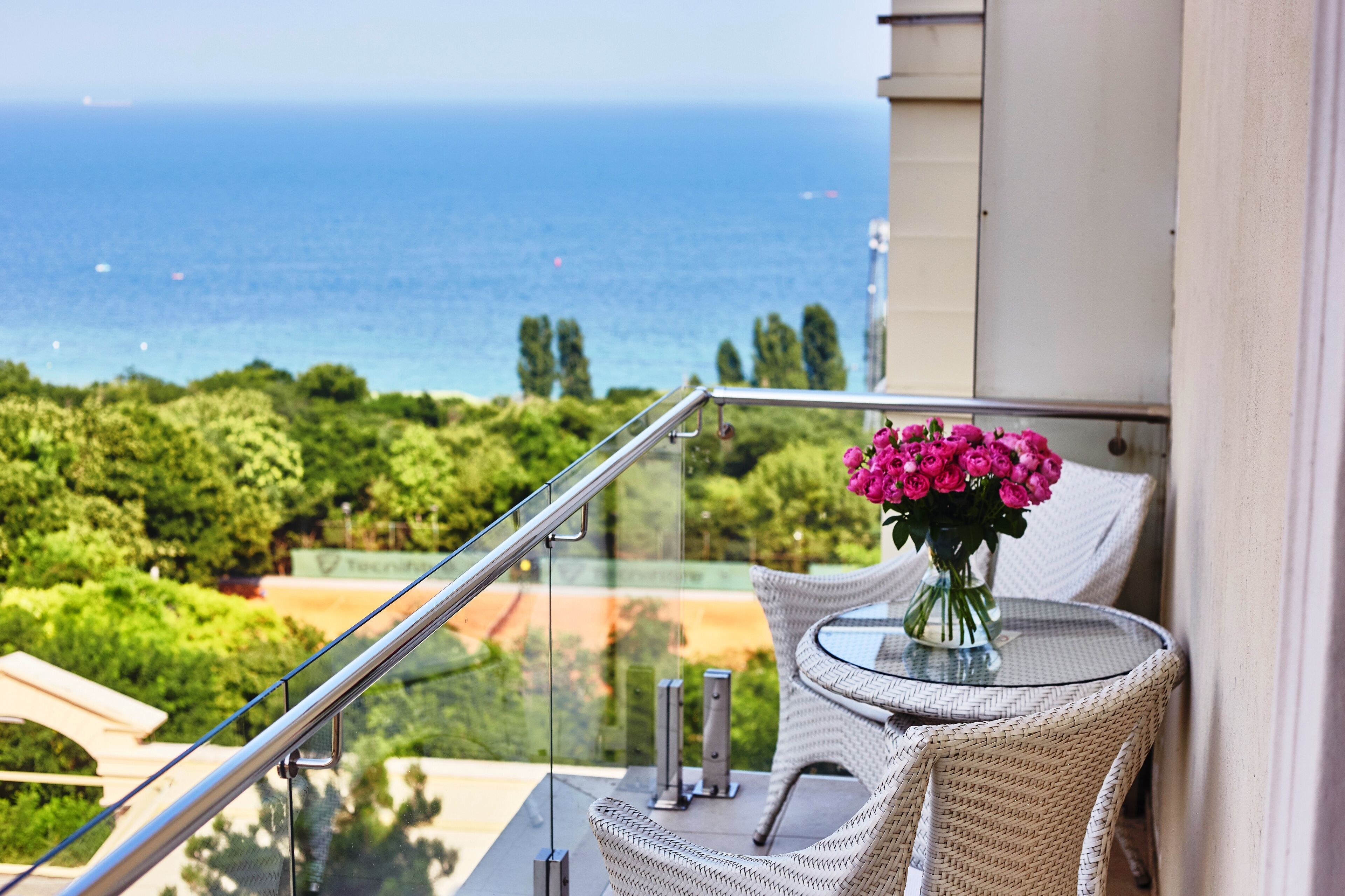 Un balcone con ringhiera in vetro che si affaccia su una vista panoramica del mare e del verde.