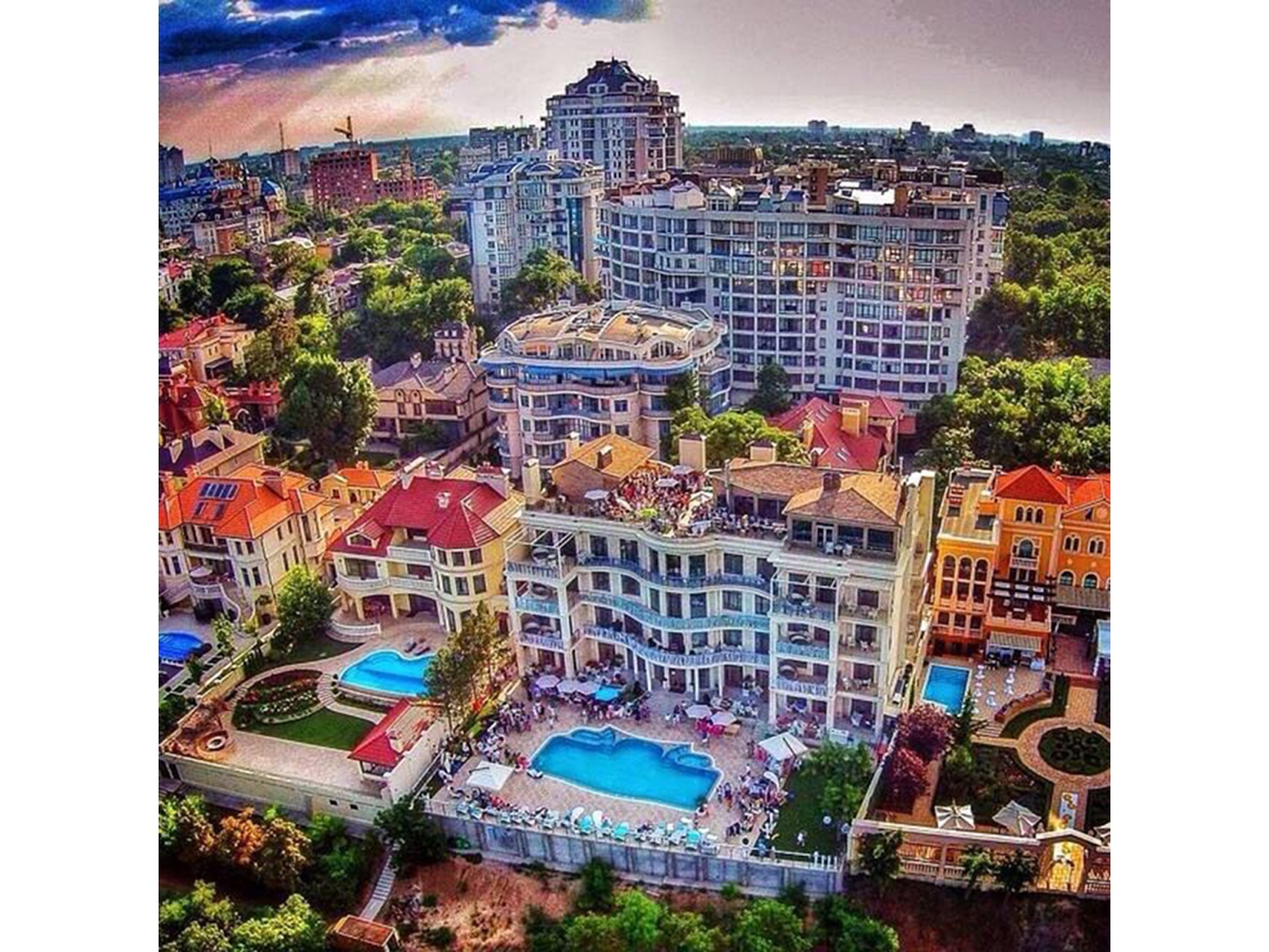 An aerial view of a hotel complex with multiple buildings, a central pool area, and surrounding greenery.