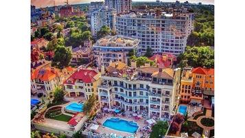 An aerial view of a hotel complex with multiple buildings, a central pool area, and surrounding greenery.