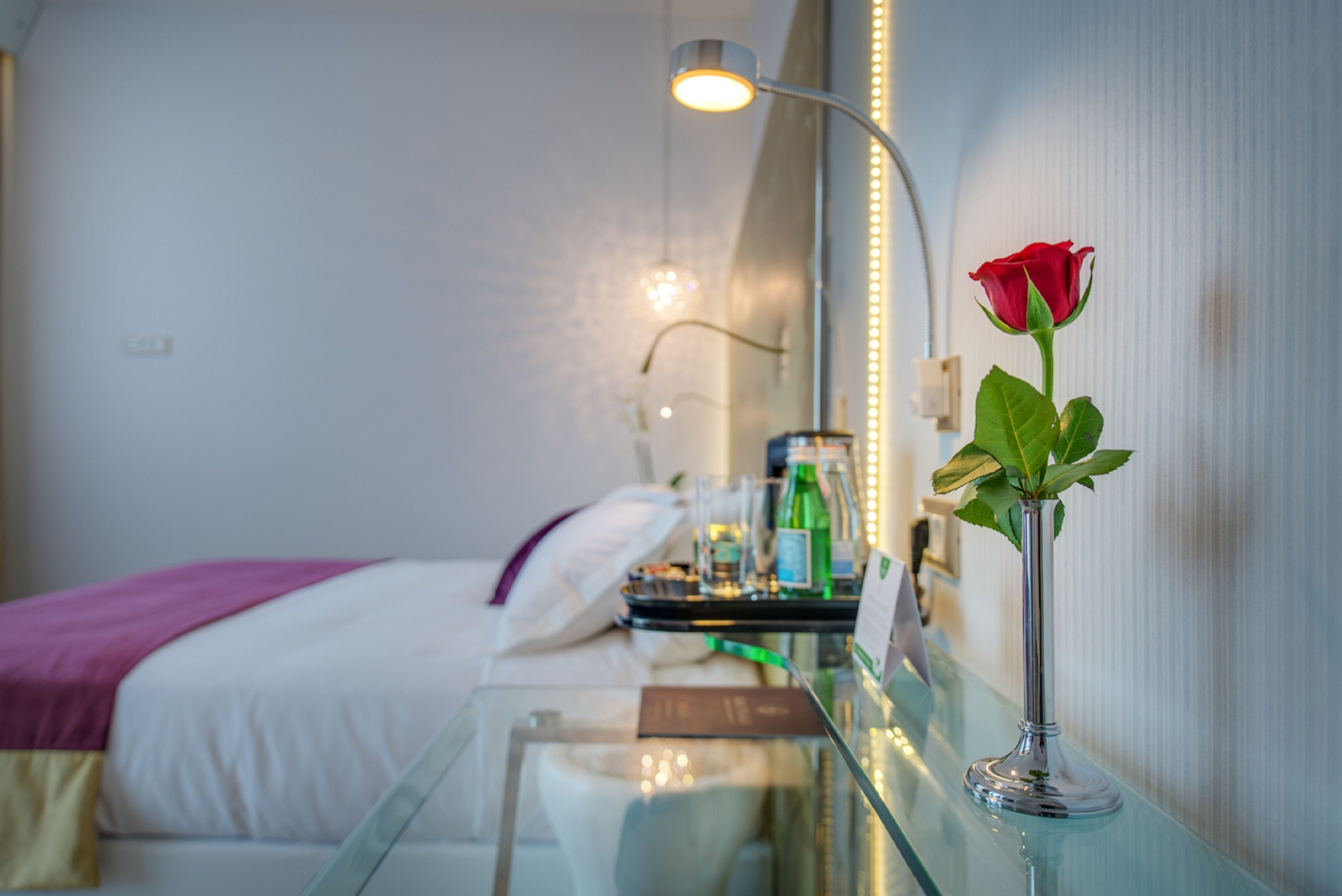 Une chambre d’hôtel avec un lit, une table de chevet et un vase contenant une seule rose rouge.