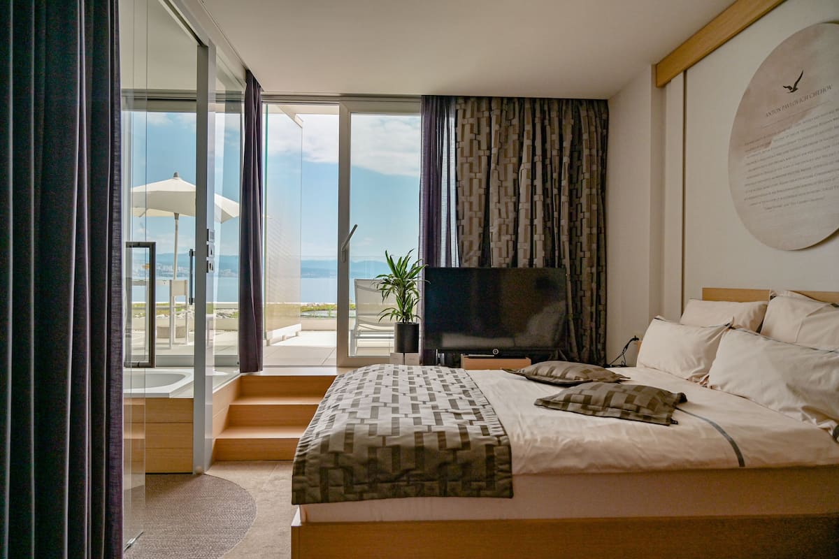 A modern hotel room with a large bed, a flat-screen TV, and a balcony with a view of the city.